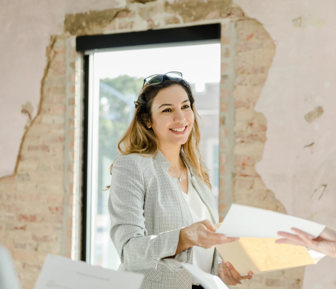 Smiling woman holding documents near window.