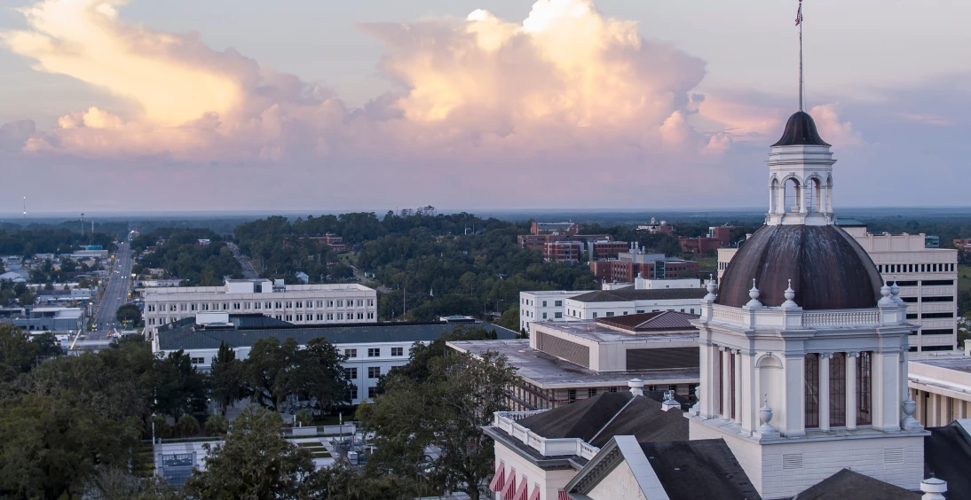 Capitol building with cityscape and sunset clouds.